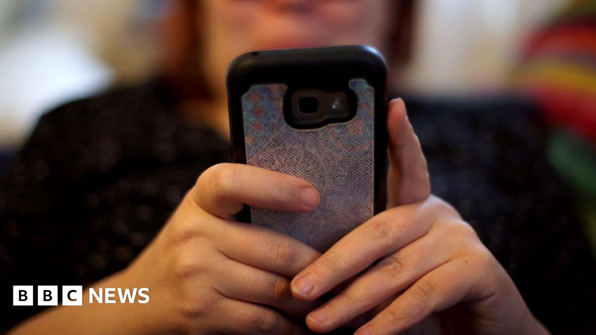 Stock image of a person on their phone. Their body and face is blurred but the back of their phone and hands are in focus.