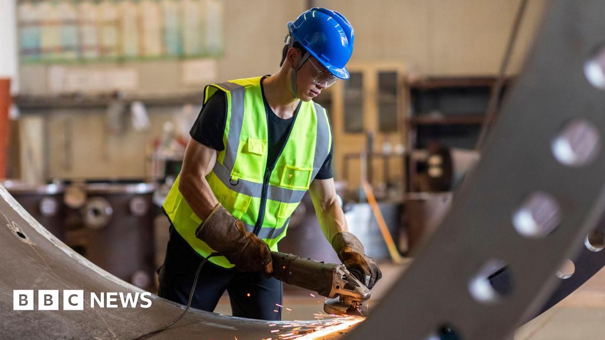 Manual worker on a workshop grinding big steel pipe

