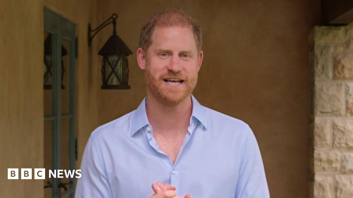 Prince Harry in a light purple shirt in front of a stone wall