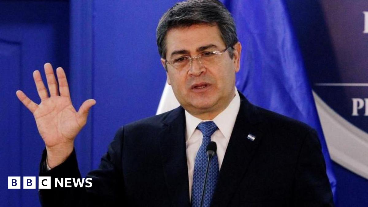 Honduras' President Juan Orlando Hernandez speaks at the Presidential House in Tegucigalpa, Honduras in January 2020. He is wearing a suit and navy blue tie, behind him is a royal blue backdrop. He is gesturing with his right hand. 