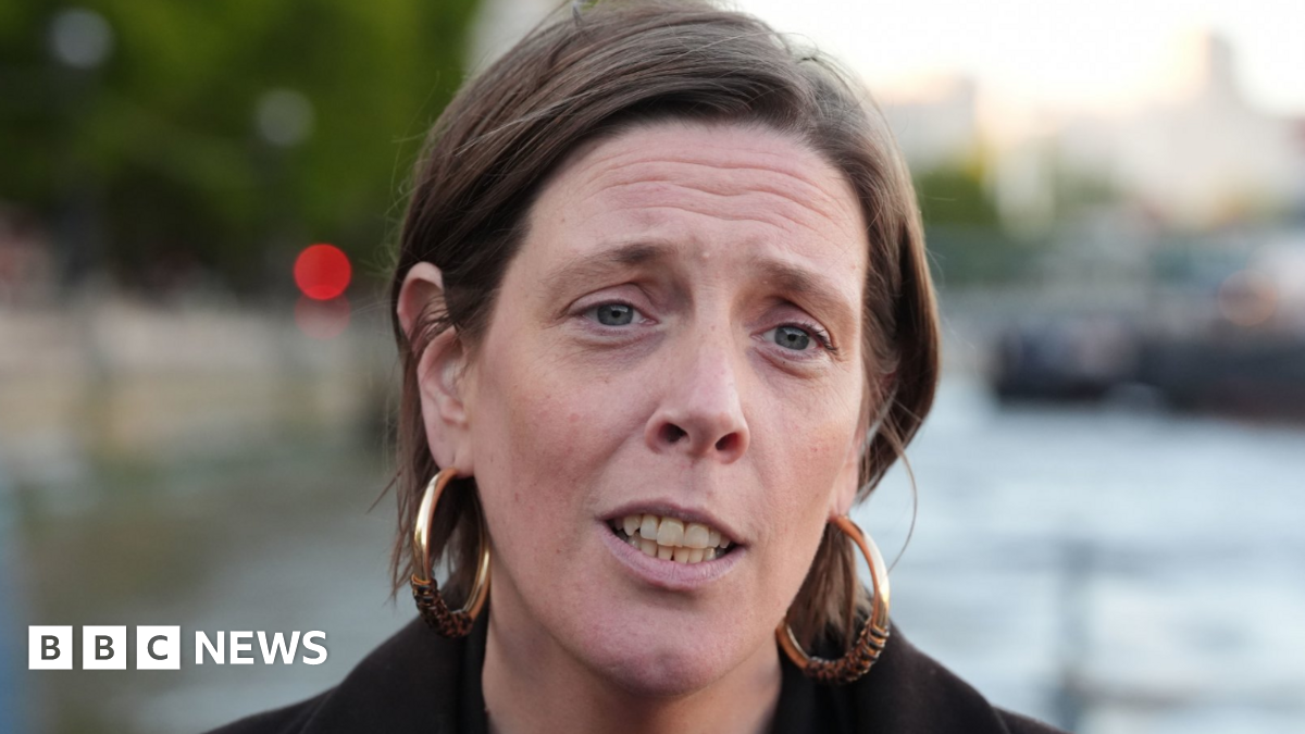 Headshot of Home Office Minister Jess Phillips. She has her short, light brown hair tucked behind her ears. She wears a thick black, jacket and very large gold hoop earrings. 