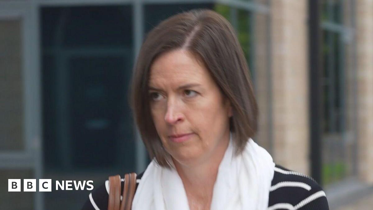 Dr Kate Searle - a woman with brunette hair just above her shoulders and wearing a black and white striped top - arrives at a tribunal. She has a white scarf on and a brown handbag over one shoulder