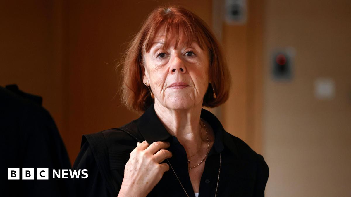 Gisèle Pelicot, a woman with red hair in a black top, looks at the camera. She is not smiling