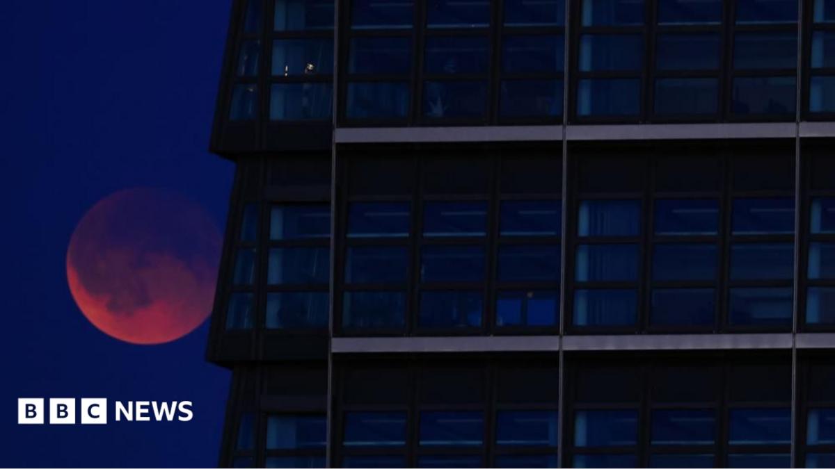 A red Moon lurking behind a glass skyscraper