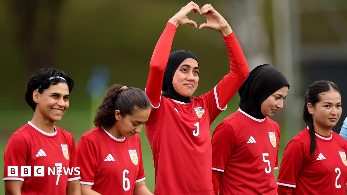 Photo: bbc.co.uk Five women in red football kit stand in a line. The one in the middle is holding her arms above her head and her hands form
