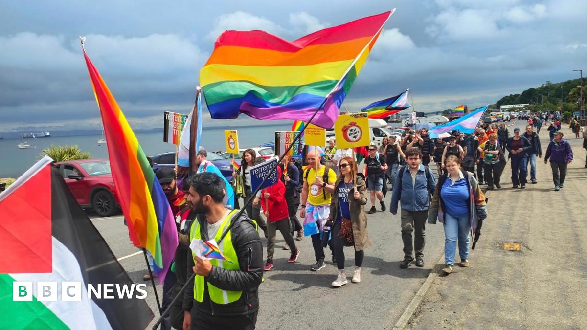 A general view of the Pride march in Brodick with a number of people carrying rainbow flags.
