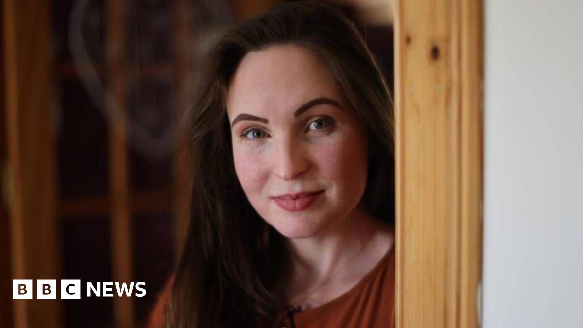 Sara Spencer standing next to a door frame. She has long brown hair and is slightly smiling at the camera.