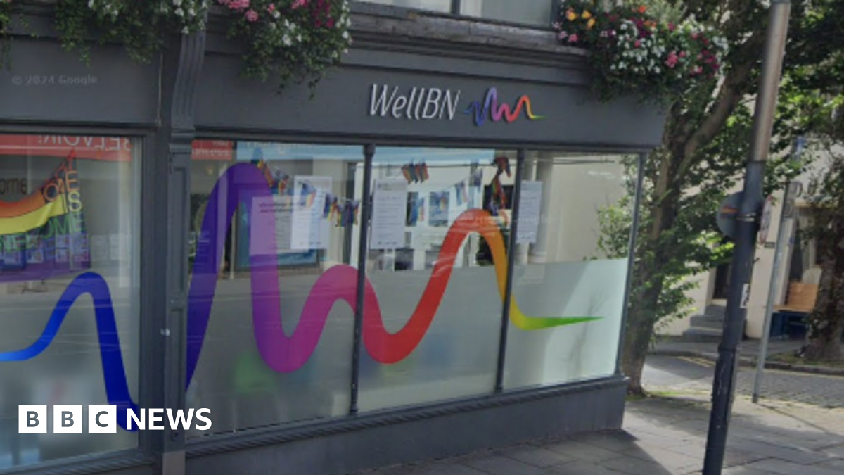 The outside of WellBN in Brighton. It is a grey-painted building with half-frosted windows and a rainbow wiggly line - its logo - on the sign. 