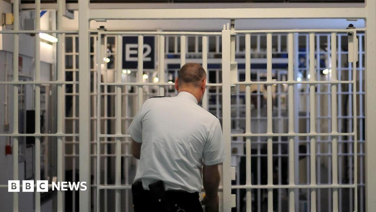 Male prison guard locks a white internal prison door. His back is to the camera.