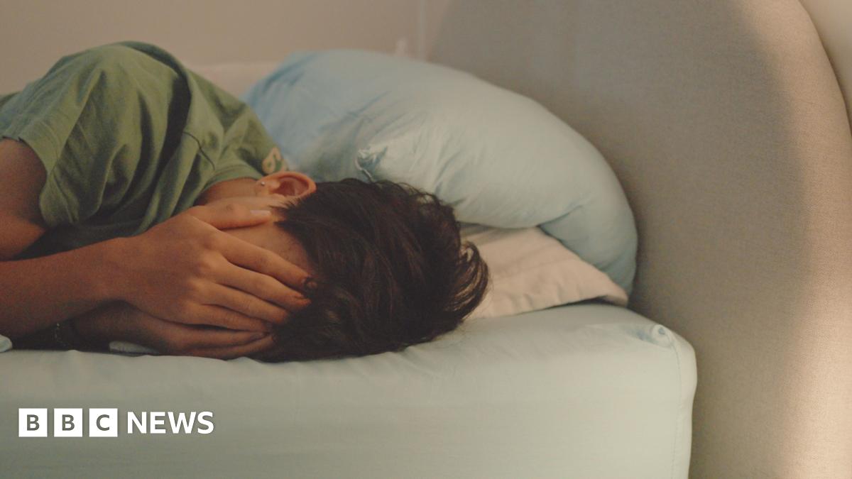 A boy holding his face appearing to cry while lying in bed.