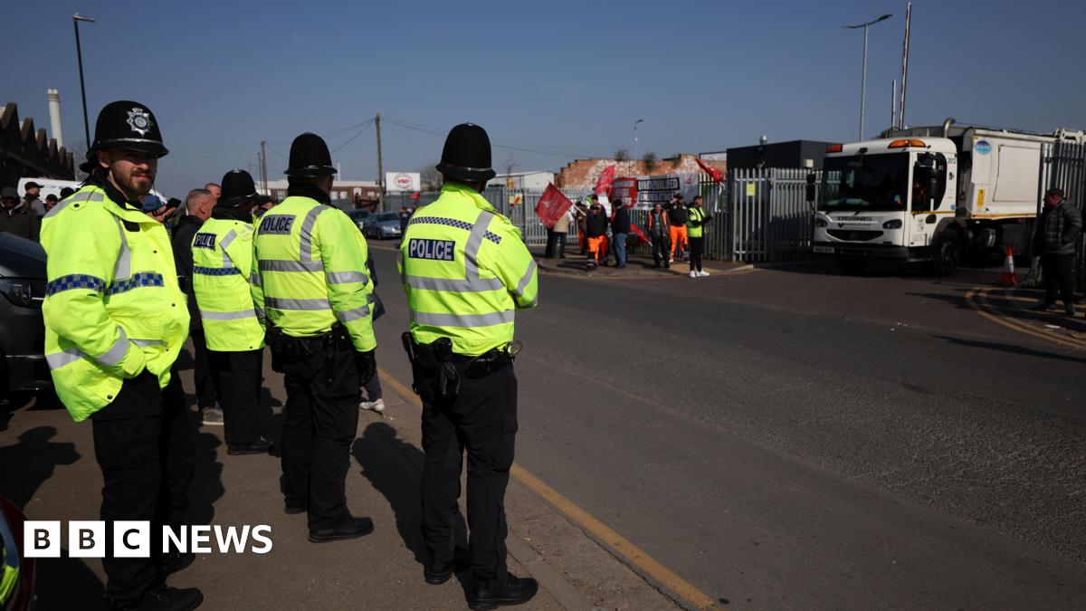Police on a picket line at a Birmingham waste depot in April. They are wearing uniform and there is a bin lorry behind them as well as a couple of protestors. It is a bright and sunny day. 