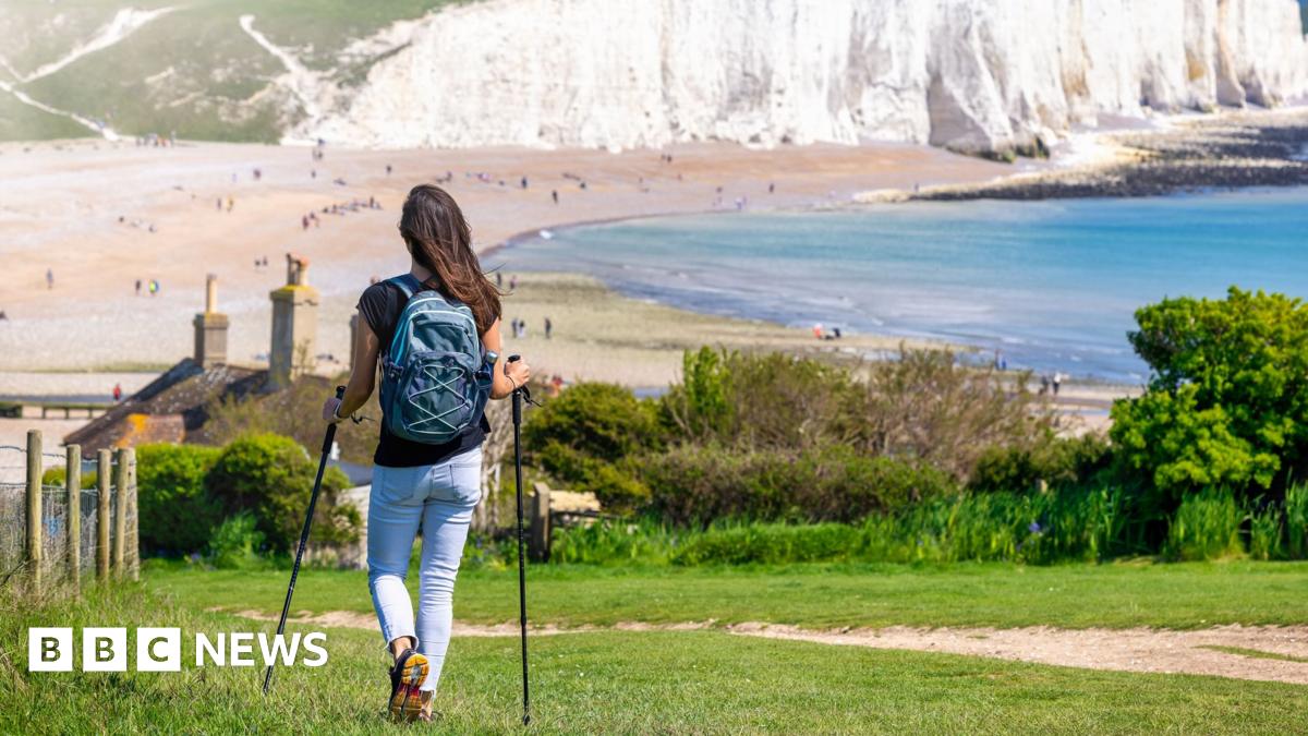 A woman hikes over green fields at the Seven Sisters Cliffs in Sussex, England, during a sunny spring day