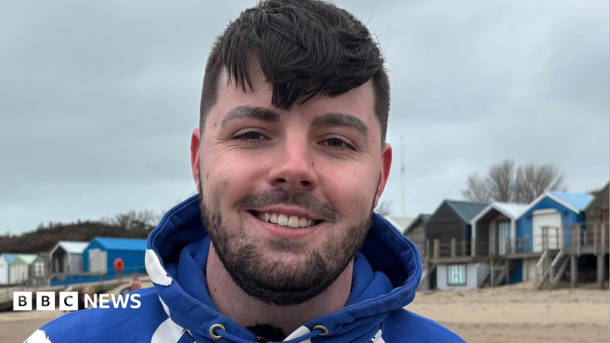 Photo: BBC Ruben smiling at the camera, wearing a blue hoodie in front of a row of beach houses