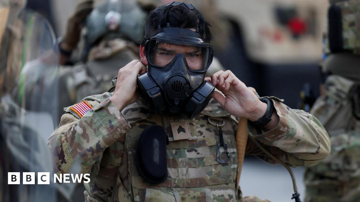 California National Guard member in camouflage colored uniform puts on black gas mask
