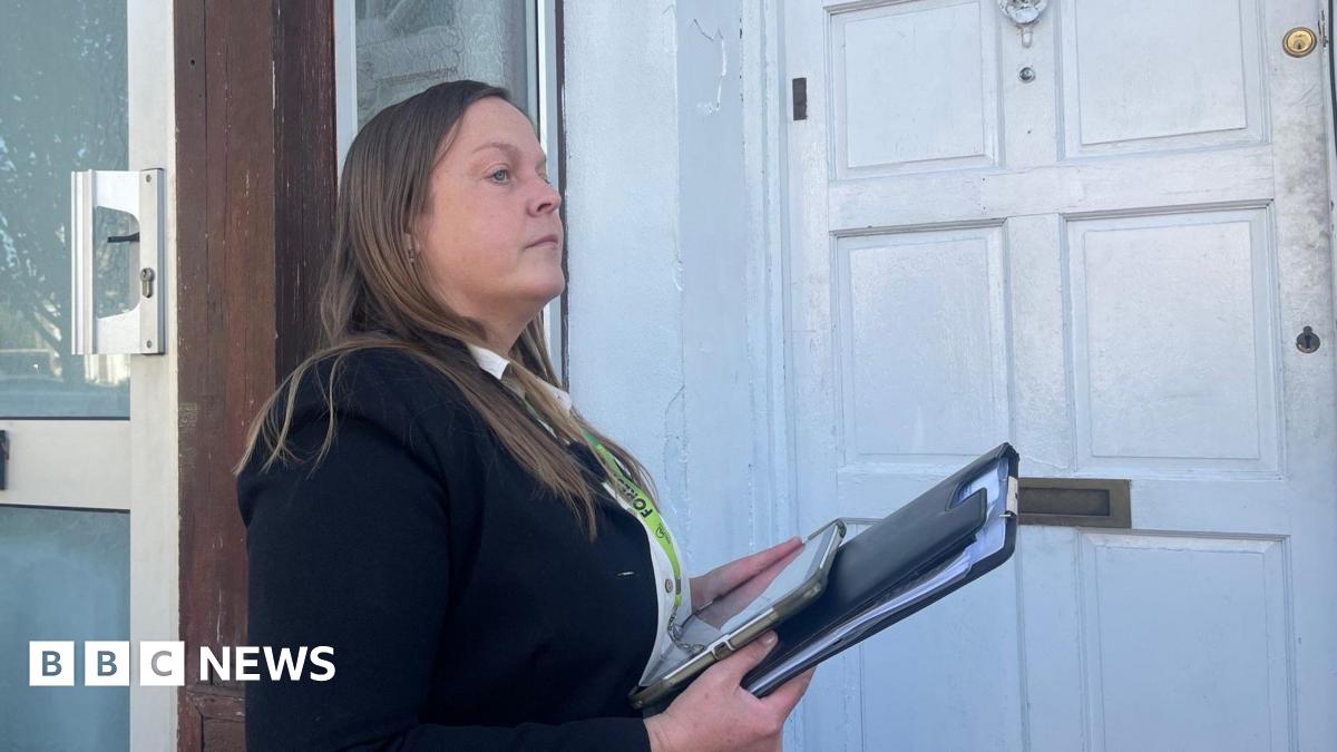 A woman with a clipboard and lanyard outside a white-painted wooden door.