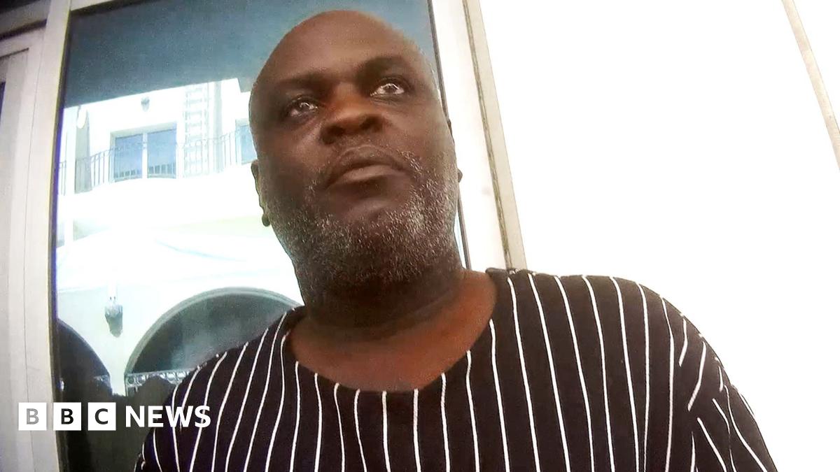 Charles Mwesigwa wearing a black shirt with while stripes by being filmed by an undercover reporter