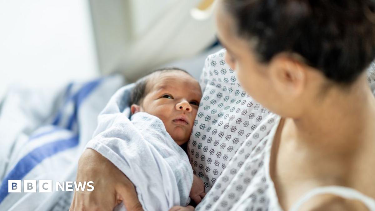 A woman cradles her newborn baby in her arms, wearing a hospital gown