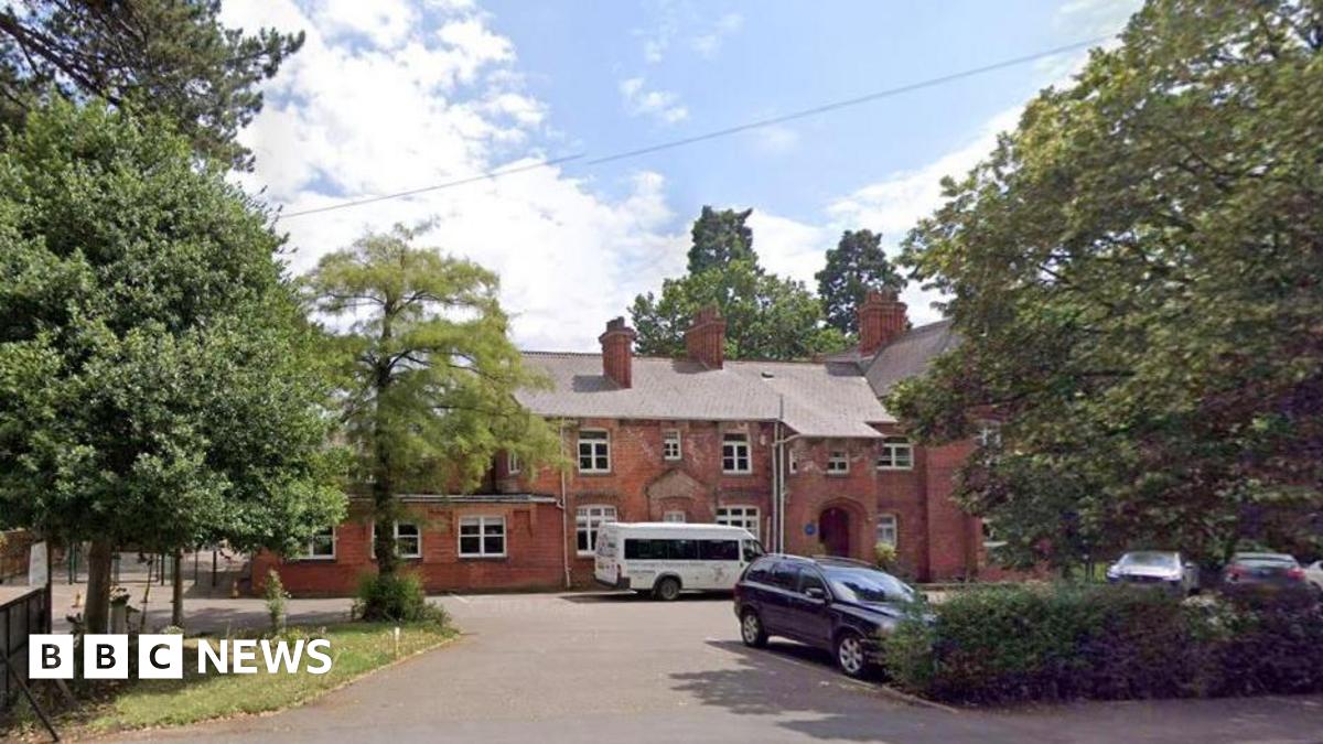 Google view of the exterior of the red-bricked school. There are cars in the foreground and the building is surrounded by trees.