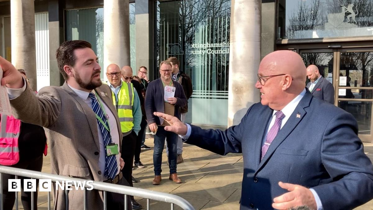 Two men in suits appear to be rowing behind a metal barrier