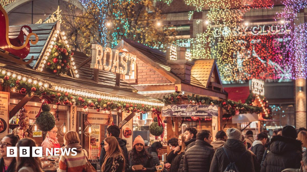 Broadgate, Coventry city centre. Christmas decorations and lights are everywhere. People are ordering food from stalls. It is winter and they have warm clothes on. 