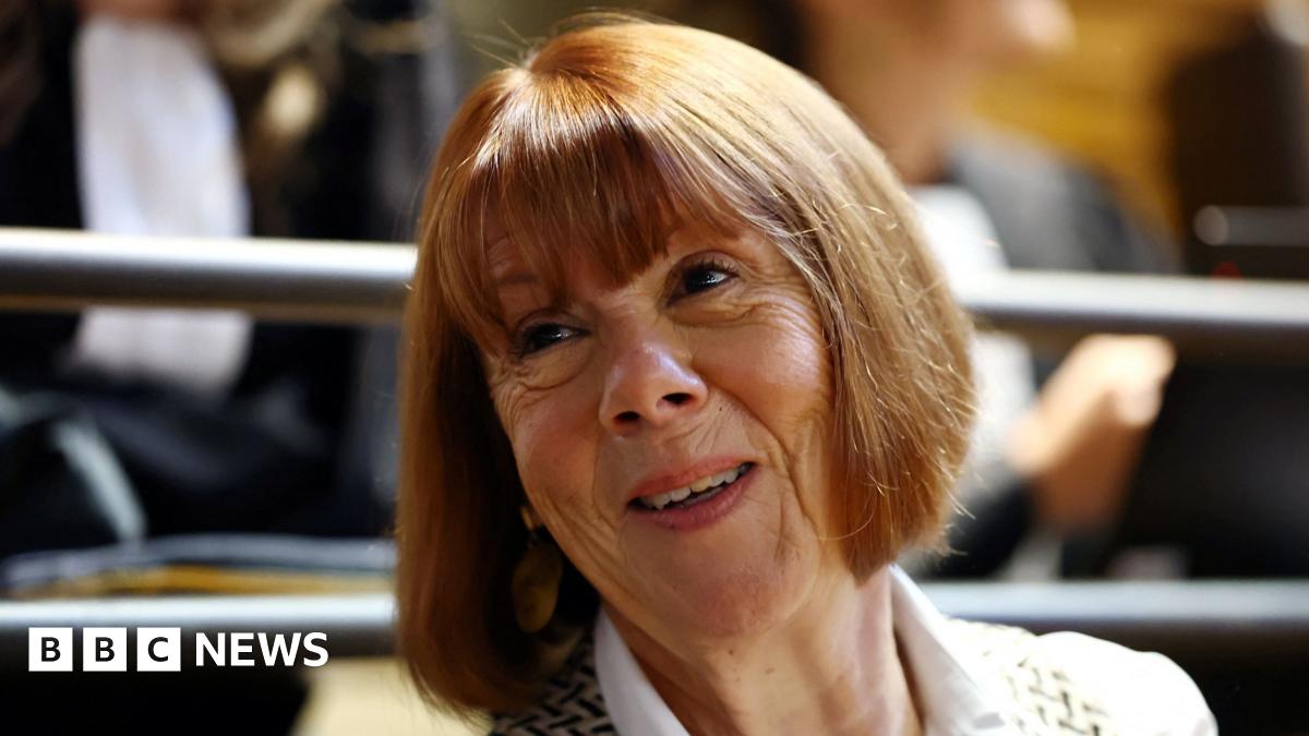 A woman with red-coloured hair and a fringe smiles