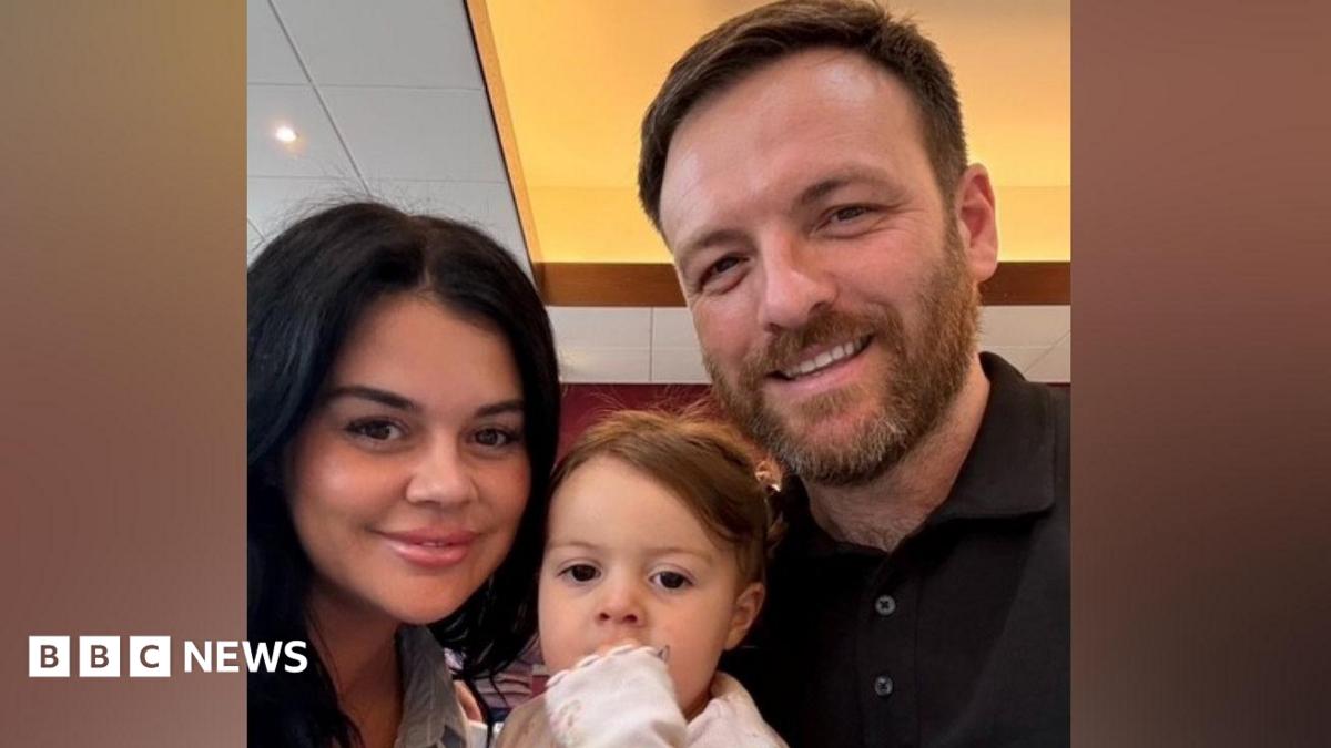 Jody is holding up her daughter and standing next to her partner in this selfie photo. 