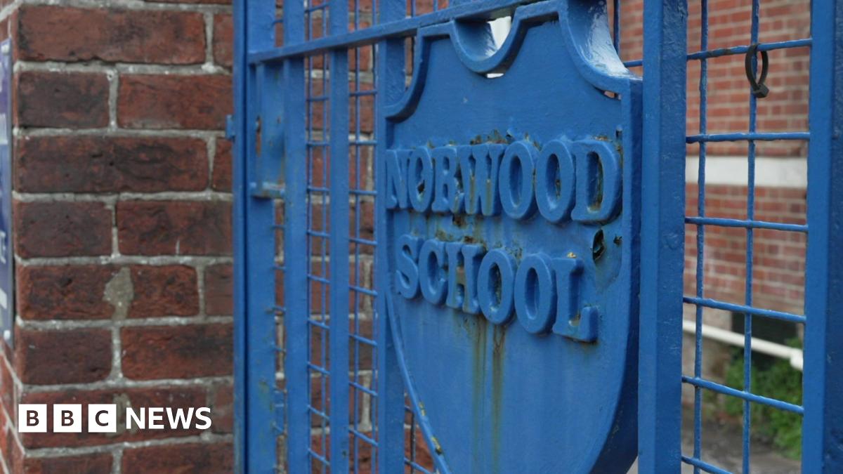 A blue metal gate with a large blue badge with the words 'Norwood School' inscribed on it.