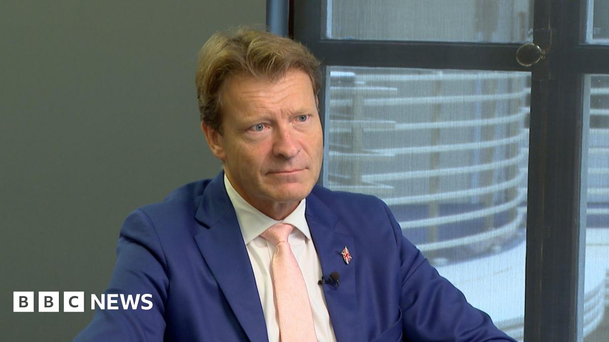 Richard Tice, Deputy Leader of Reform UK, sitting in the BBC Millbank offices during an interview with BBC South East. Looking off camera, wearing a blue suit with a Union Jack pin and a pink tie