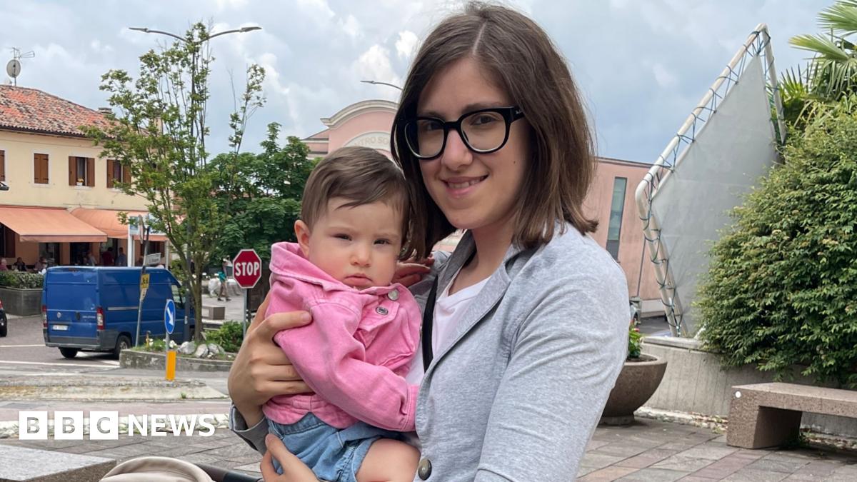 Valentina, a woman with dark hair and glasses, holds a baby in a pink jumper