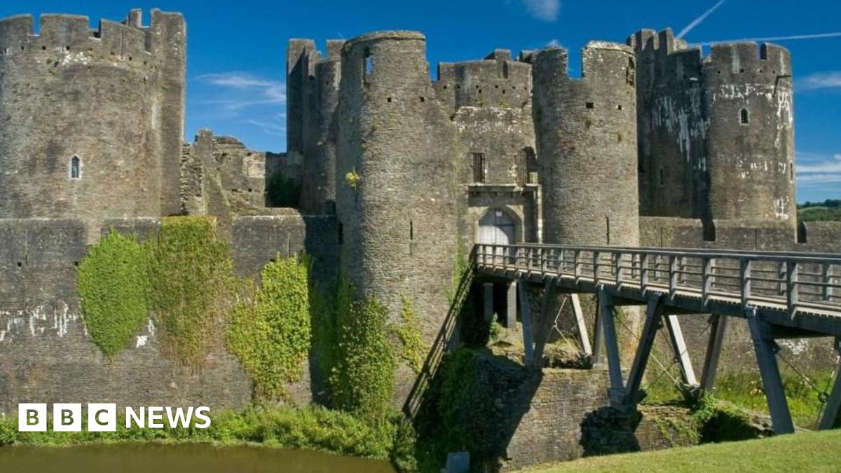 A general view of Caerphilly castle with a moat in the foreground, and a bridge across it.