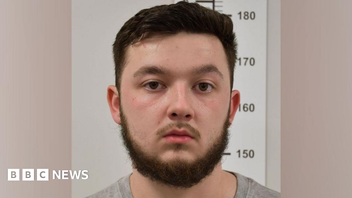 Dylan Earl wears a grey shirt and blank expression with short brown hair and a beard