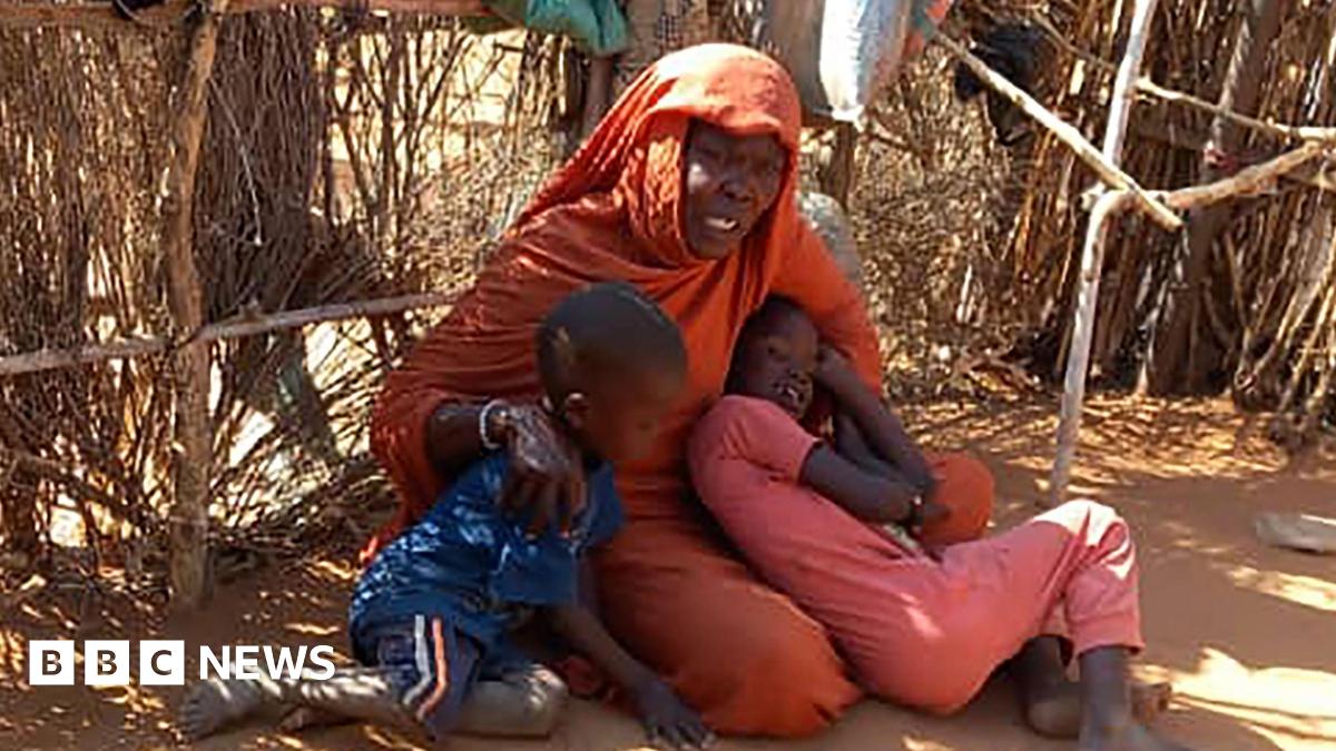 A woman hold two children. She is wearing an orange gown and headscarf