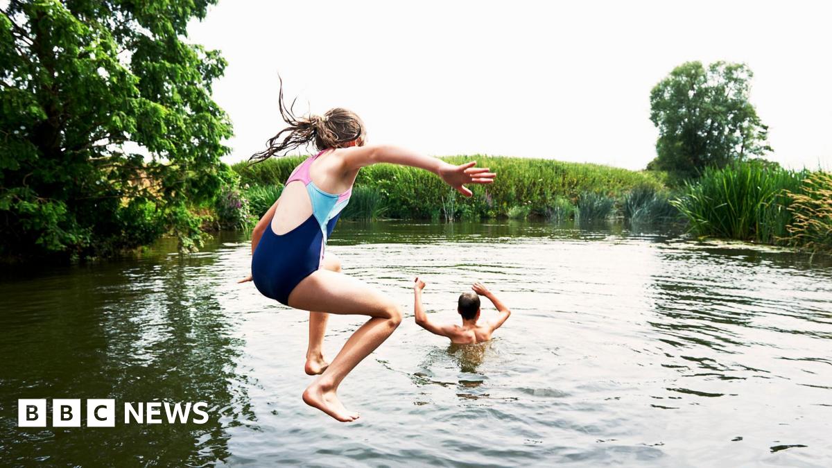 A boy and a girl jumping into a lake surrounded by trees and reeds