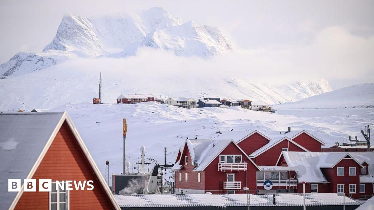 red homes with snow-covered roofs sit in a valley with icy-covered mountains in the background. 