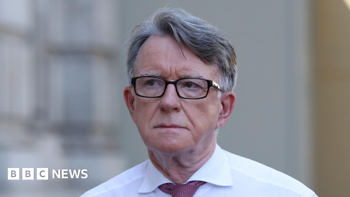 Peter Mandelson is wearing a pair of glasses and a white shirt with a red tie.