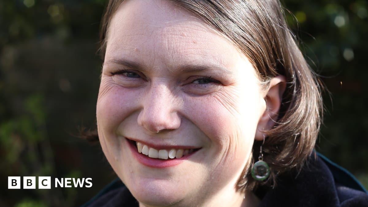 Sarah Wakefield has shoulder length brown hair and is wearing green earrings.