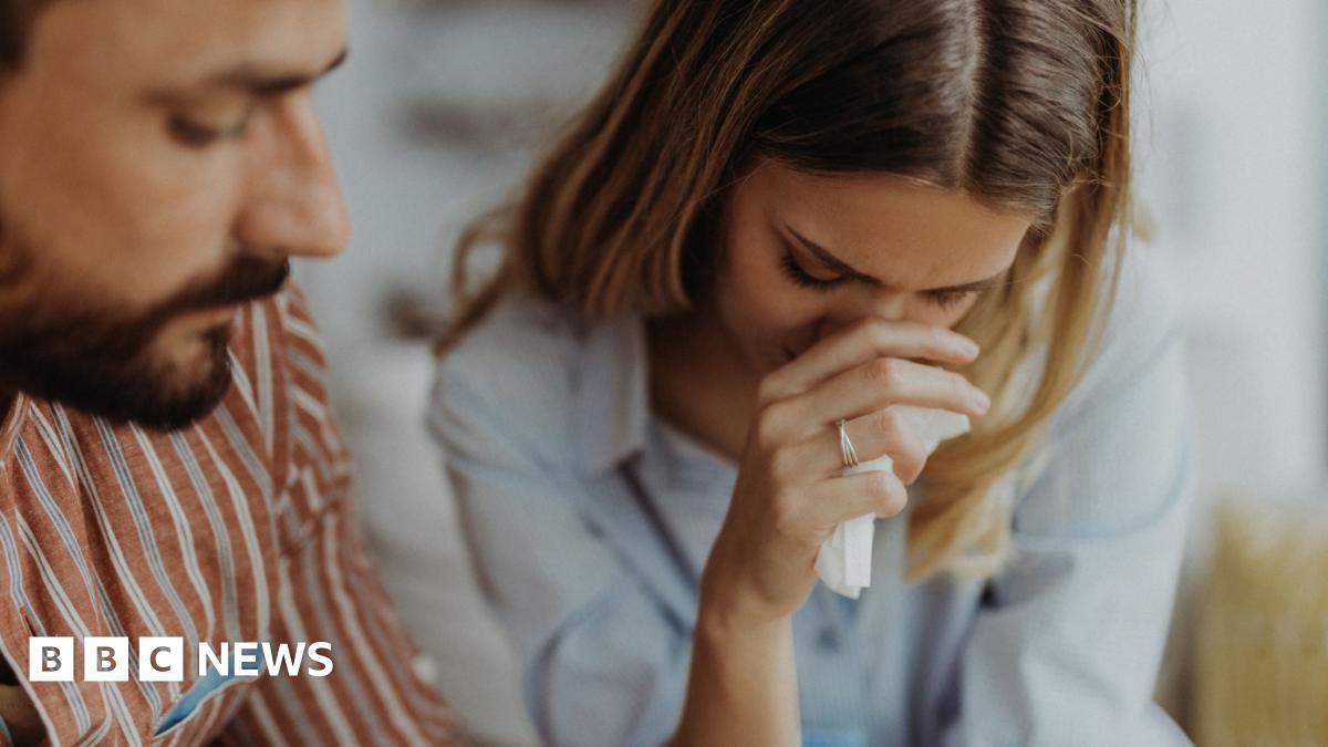 A close up stock photo shows an emotional couple crying at home.
