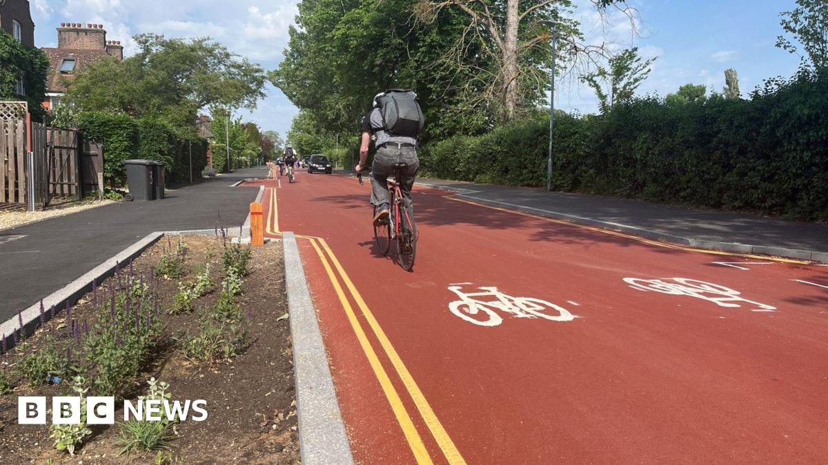 General view of Adams Road, which is a red road with double yellow lines, cycles painted on to the road and a cyclist on it.
