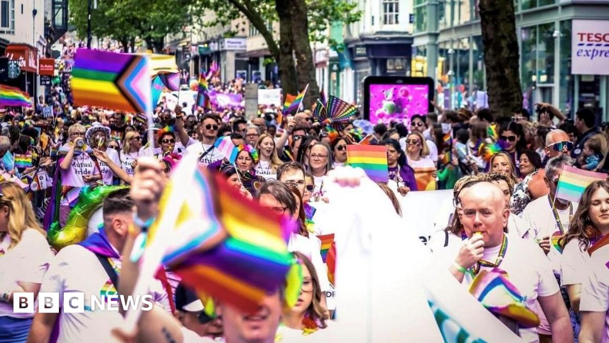 People marching in the 2024 Birmingham Pride parade, through the city centre, Many are carrying rainbow flags and some are blowing whistles. 
