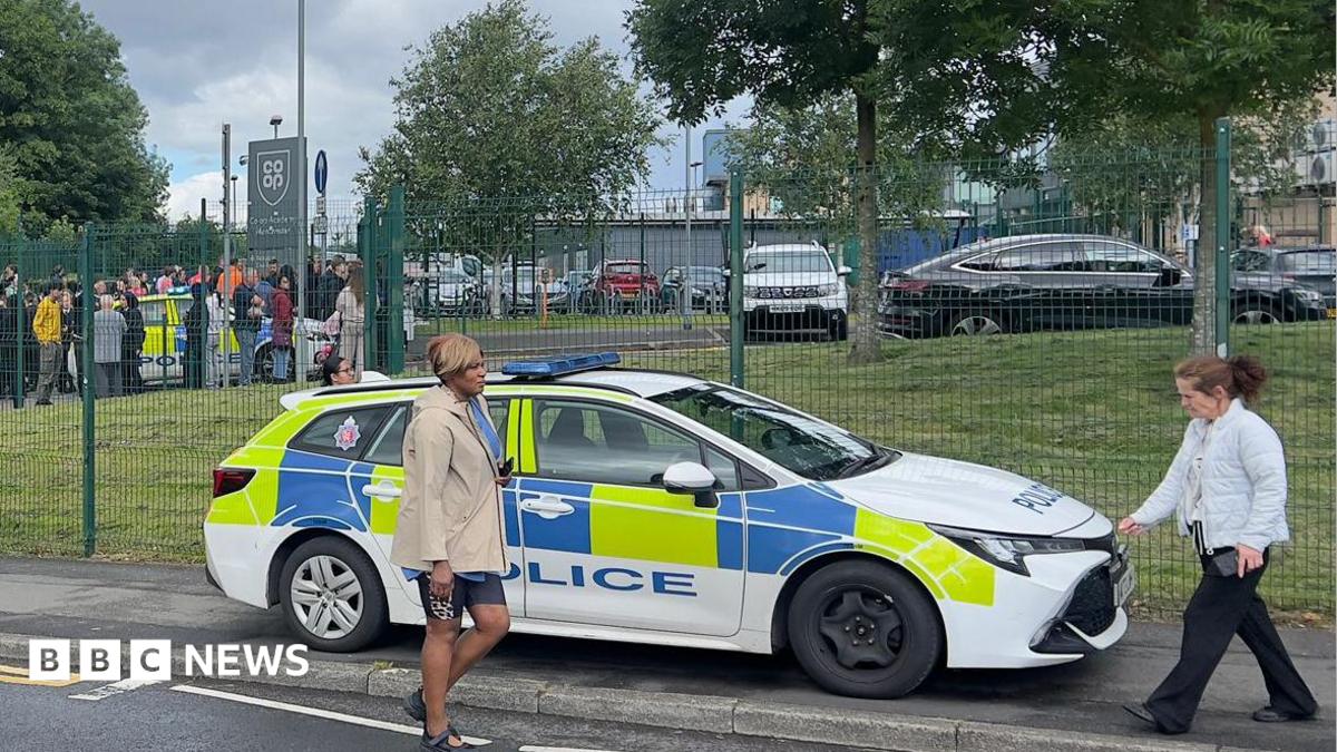 A police car parked outside a school as people walk past. 