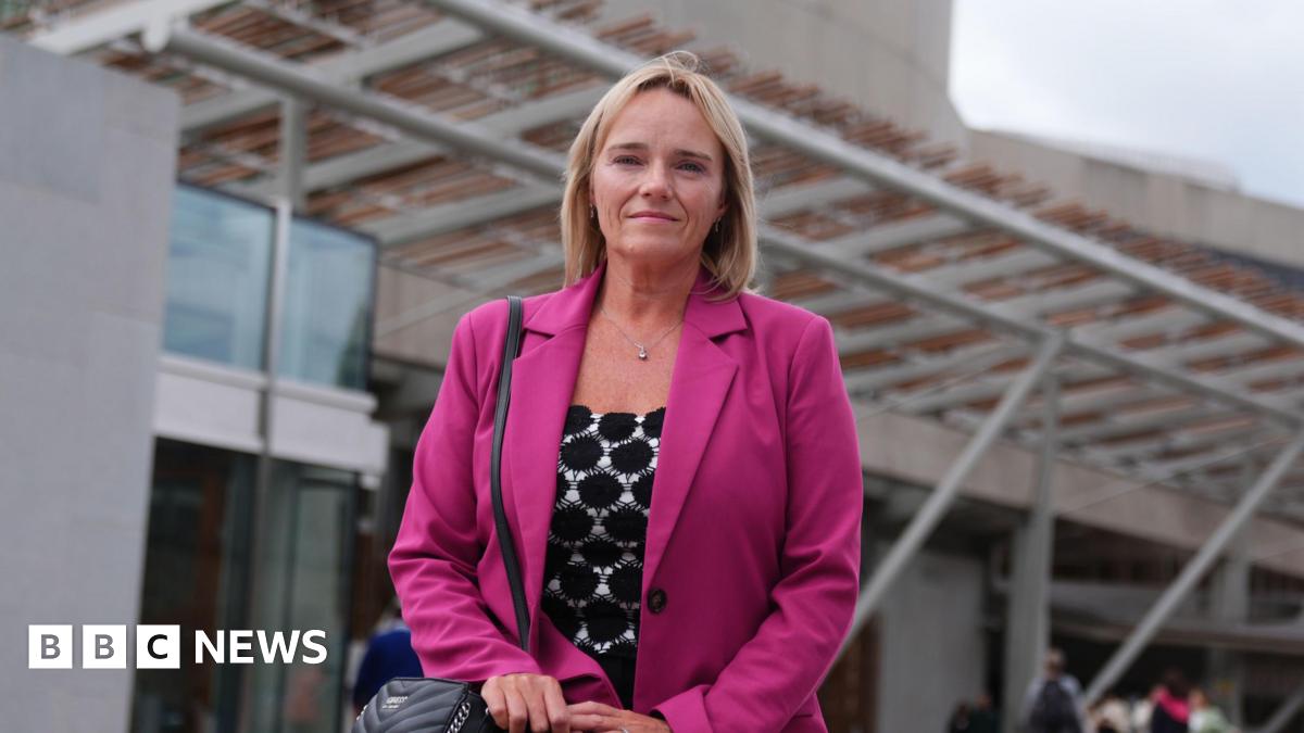 Sandie Peggie wearing a pink jacket and with short blonde hair, outside the entrance to the Scottish Parliament building