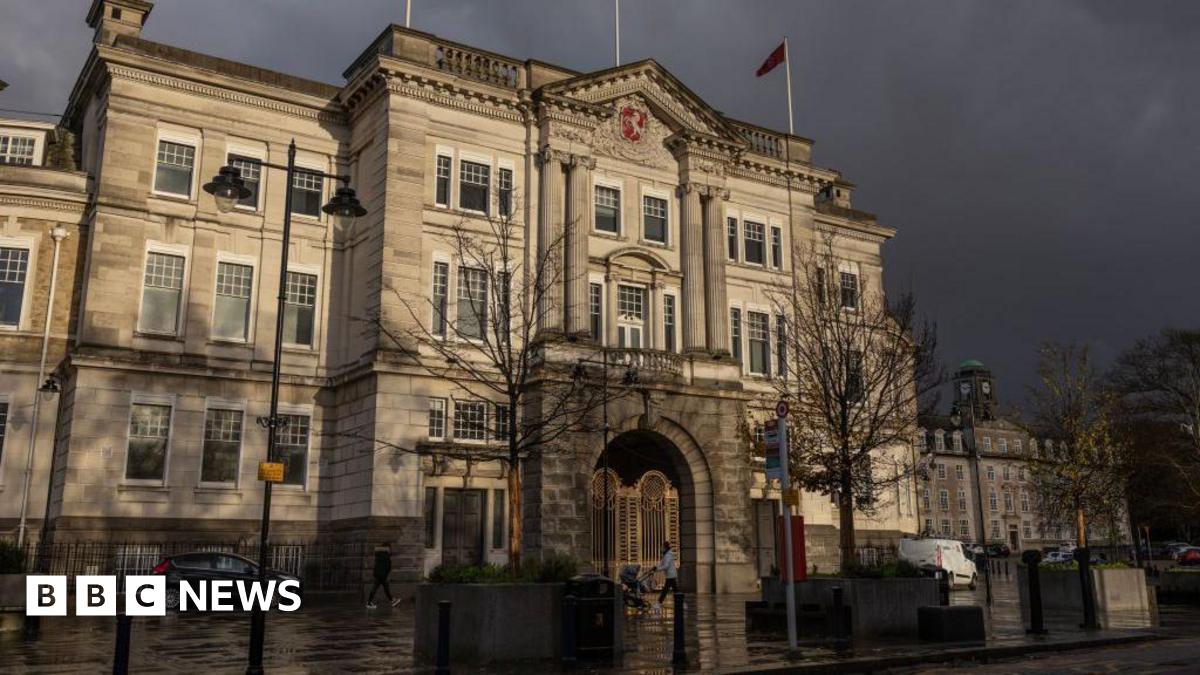 County Hall in Maidstone, which is a large and grand stone building. Dark clouds are gathering in the sky above the building.