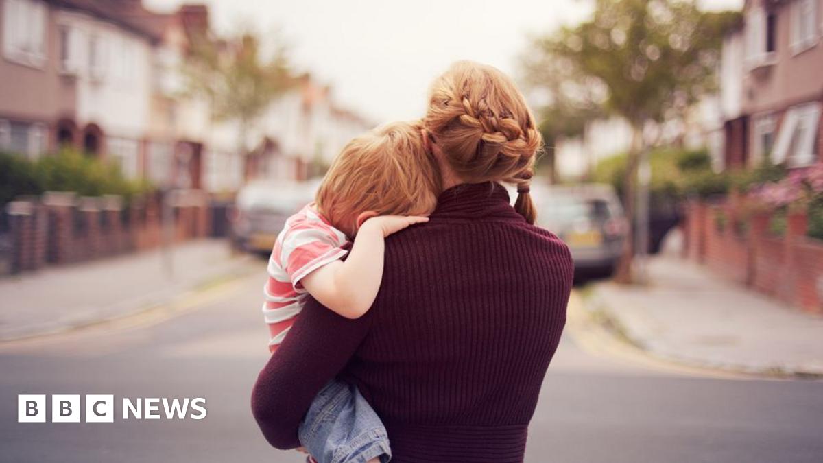 Rear view of a woman carrying a child in a street. Their faces are hidden.