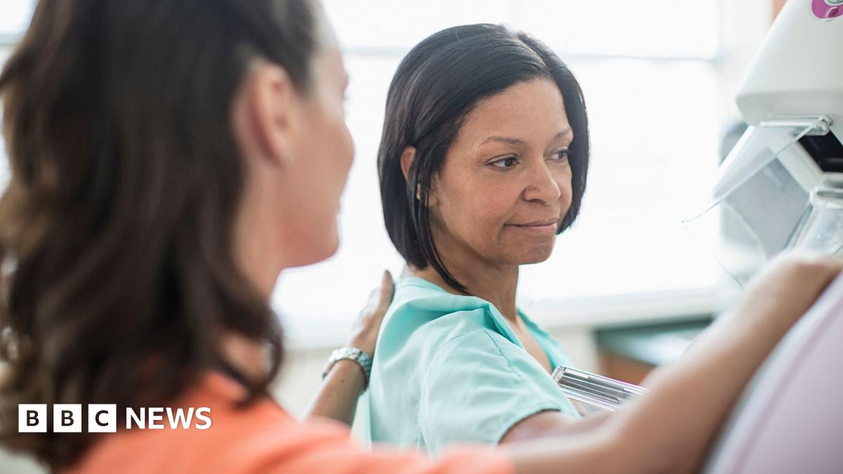 A woman goes for a mammogram.  She is pictured alongside a female medical professional. 