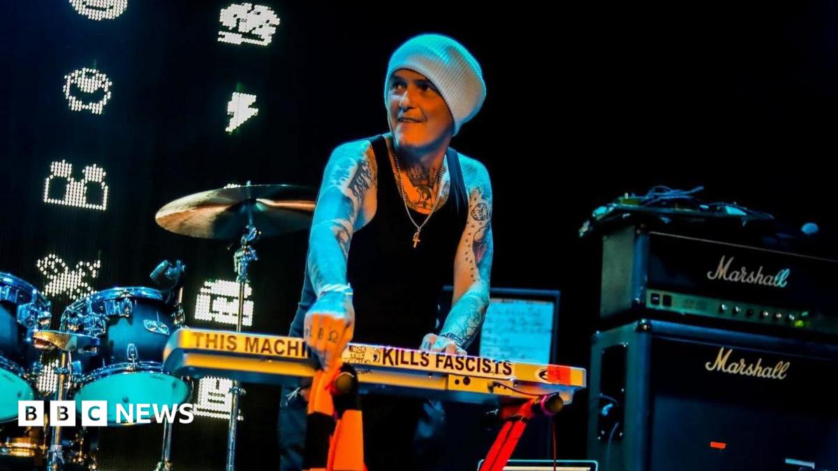 Photo: bbc.co.uk Derry Brownson, the keyboardist of EMF, smiles as he performs on stage. He is wearing a grey beanie, a black tank top and