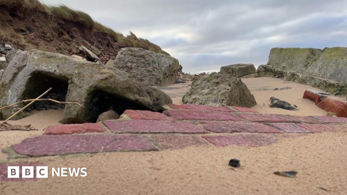 Remnants of a red brick wall sunken in sand and rocks