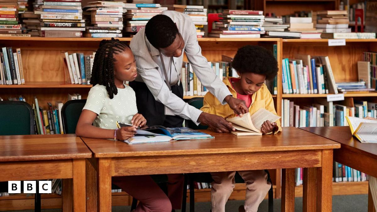 Two children look at books in library with an adult.