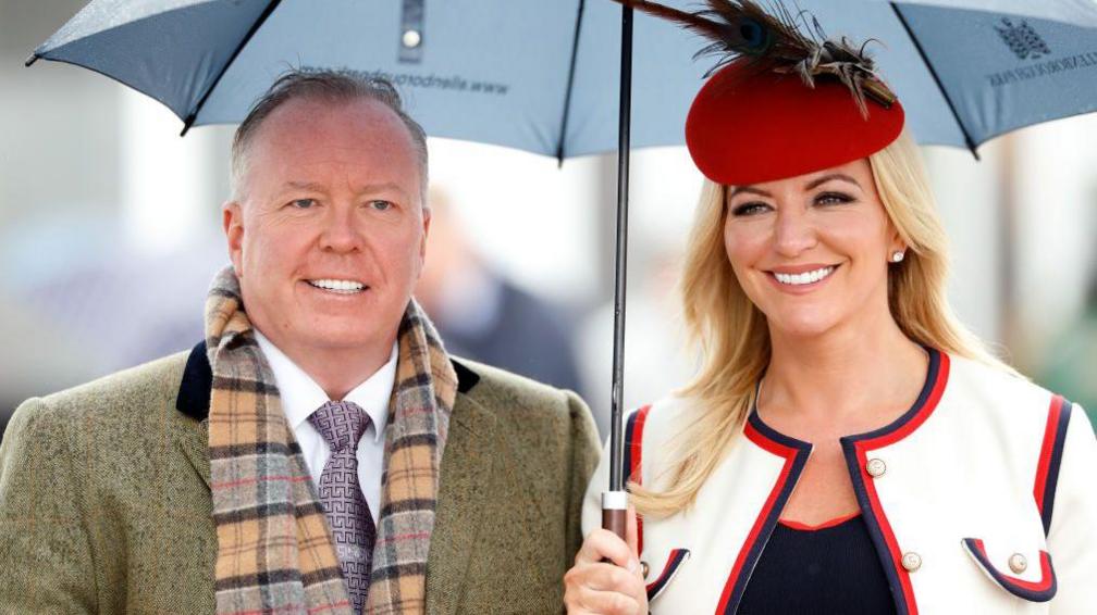 Michelle Mone pictured standing under an umberella next to her husband, Doug Barrowman, attending the Cheltenham Festival in 2019