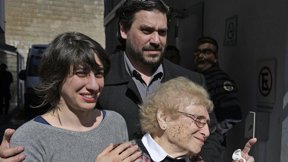Roisinblit speaks with the press next to Guillermo wearing a dark jacket nd her granddaughter Mariana Eva Perez in a grey sweater, outside the court following the reading of the sentence to former Airforce chief Omar Graffigna.