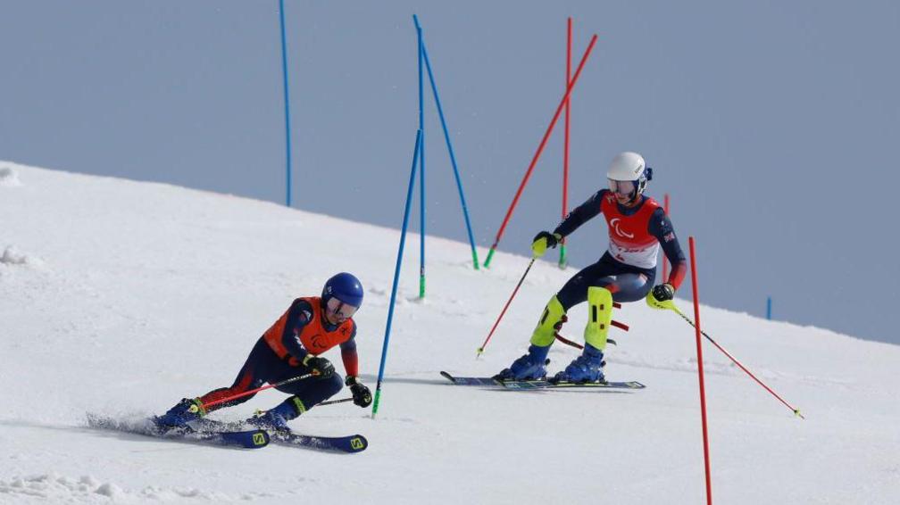 Great Britain's Neil Simpson competes in the alpine skiing with his guide Andrew who is skiing in front of him between poles down a snowy hill